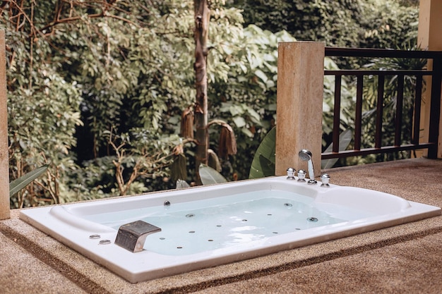 El relajante jacuzzi blanco vacío con agua se encuentra al aire libre en el fondo de una naturaleza verde y exótica. Queridas vacaciones de lujo en los trópicos. Viajar al extranjero. El concepto de vacaciones.