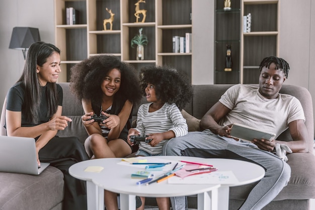 Relajarse alegres padres de familia multirraciales con dos niños sentados en el sofá sala de estar jugando videojuegos vacaciones de ocio juntos