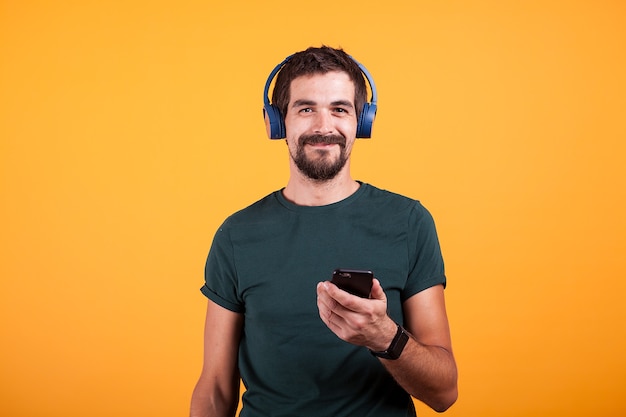 Relajarse a hombre atractivo con auriculares azules y smartphone en sus manos sobre fondo naranja en estudio