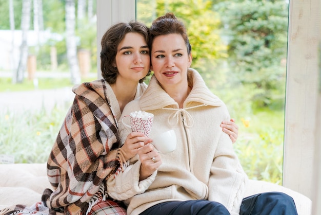 Relájese riendo y madre e hija mayores con una taza de café para el hogar