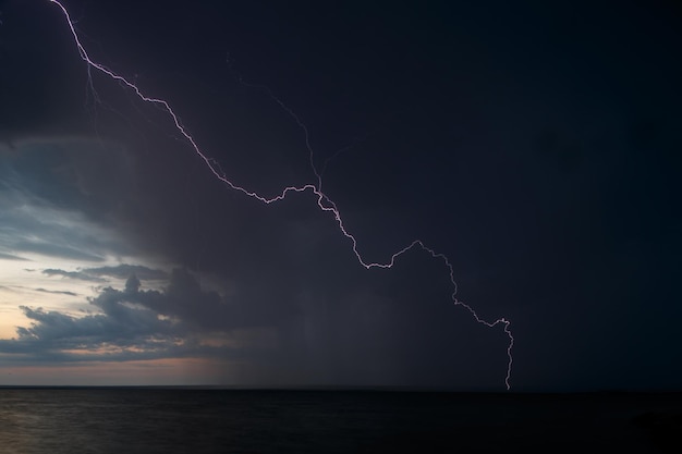 El relámpago bifurcado sobre el mar contra el cielo por la noche