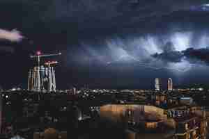 Foto relámpagos brillando sobre la ciudad de barcelona apuntando directamente al monumento de la sagrada familia. puedes ver las nubes y la tormenta.