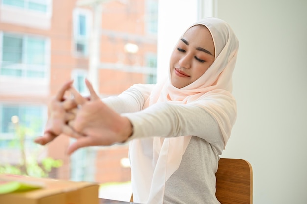 Relaxada jovem empresária muçulmana asiática usando hijab esticando os braços se sentindo cansada