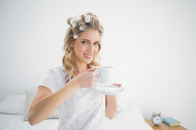 Foto relaxado bonita loira usando rolos de cabelo segurando café