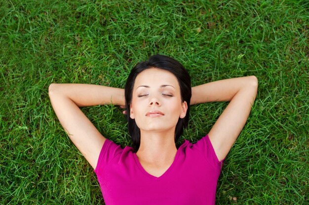 Relaxamento total. Vista superior de uma bela jovem dormindo com as mãos atrás da cabeça e deitada na grama verde