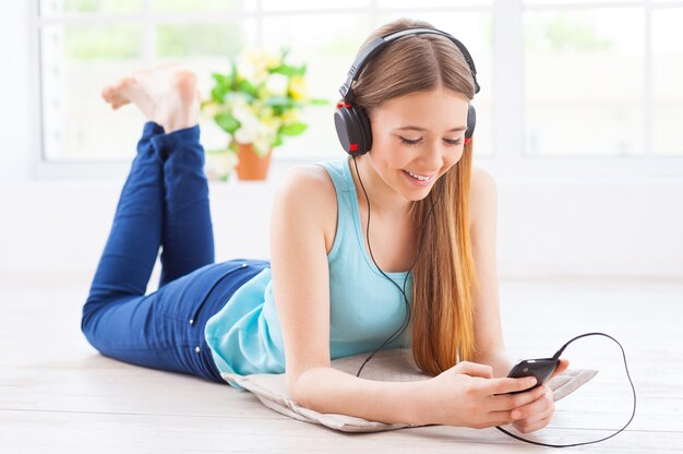 Relaxando com sua música favorita. Adolescente alegre em fones de ouvido, ouvindo música enquanto está deitada no chão de seu apartamento