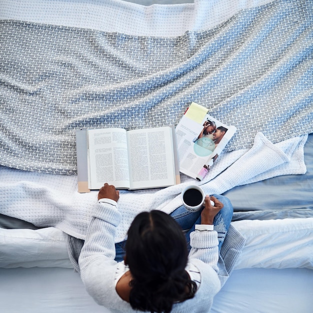 Relaxando com uma boa leitura foto de alto ângulo de uma mulher irreconhecível lendo um livro e tomando café na cama em seu quarto em casa