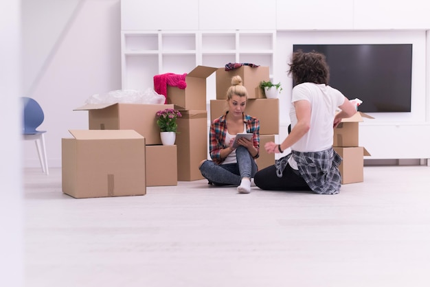 Relaxando em casa nova. Alegre casal jovem sentado no chão enquanto caixas de papelão ao redor deles