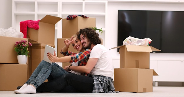 Relaxando em casa nova. Alegre casal jovem sentado no chão enquanto caixas de papelão ao redor deles