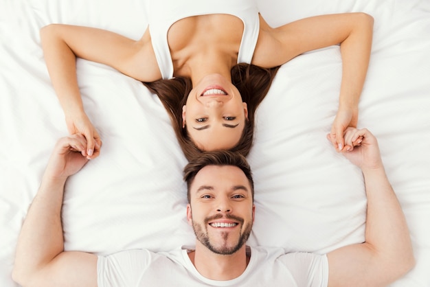 Foto relaxando na cama juntos. vista superior de um lindo jovem casal apaixonado, deitado na cama, de mãos dadas