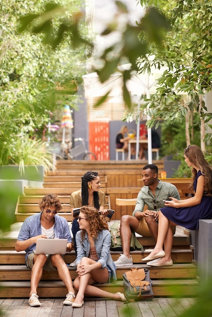 Relaxando no campus entre as aulas um grupo de jovens estudantes relaxando ao ar livre com dispositivos tecnológicos