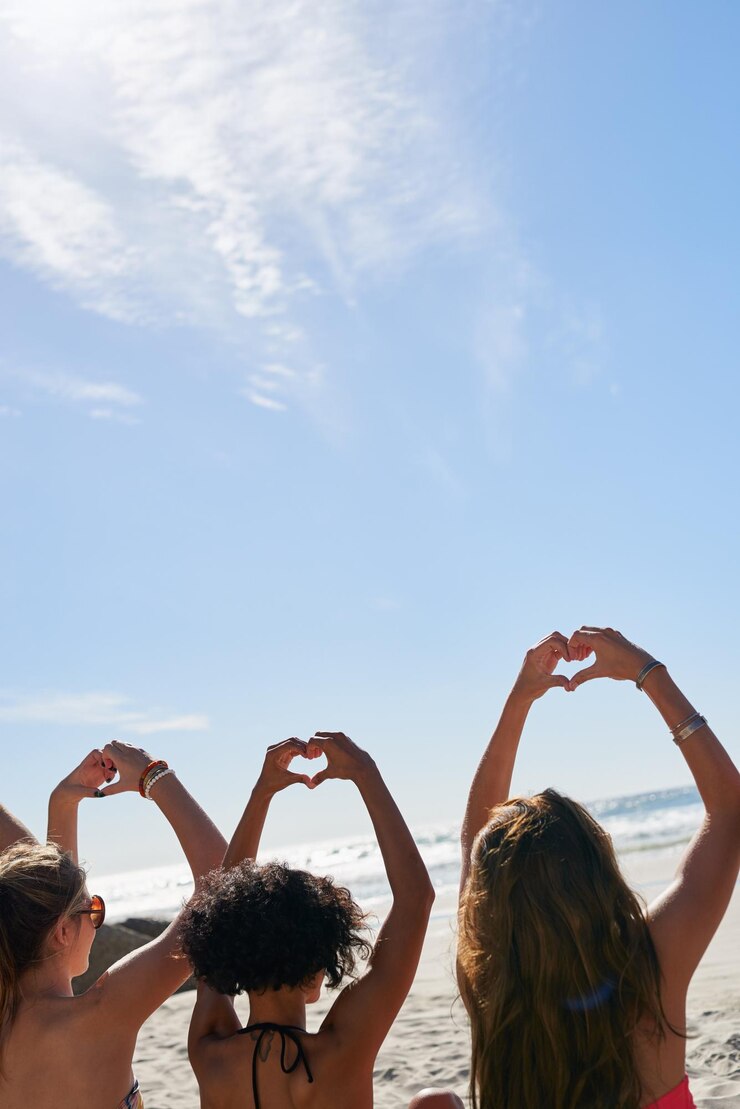 Foto relaxe as mãos no coração e amigos na praia para férias de verão férias tropicais e fim de semana ao ar livre mockup espaço céu azul e costas de mulheres pelo oceano com emoji sinal de amor e gesto para viajar