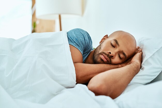 Relaxe dormindo e homem na cama em casa e bem-estar com paz confortável ou felicidade Homem africano ou cara em um quarto descanso saudável ou sonhando com conforto sonolento ou cansado com um cobertor