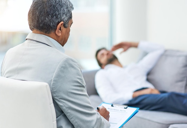 Foto relaxe e comece desde o início foto de um jovem estressado discutindo com seu médico enquanto estava deitado em um sofá dentro de um consultório médico durante o dia