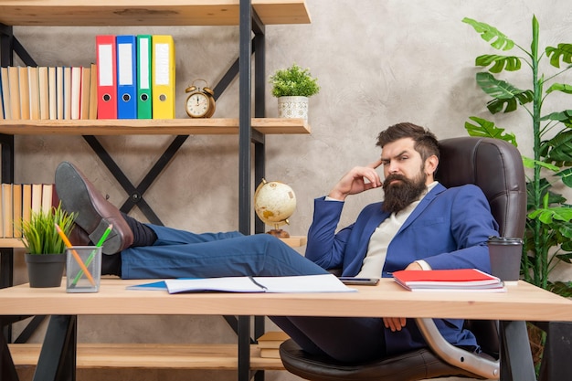Relaxe e descontraia Funcionário sério relaxa com as pernas na mesa Descanso no escritório Relaxamento que conta
