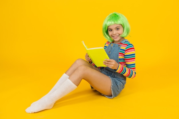 Relaxe e leia o livro. Adorável criança pequena ler livro fundo amarelo. Menina bonitinha gosta de ler. Você não pode comprar felicidade, mas pode comprar um livro. Loja de livros. Biblioteca. Bibliópola.