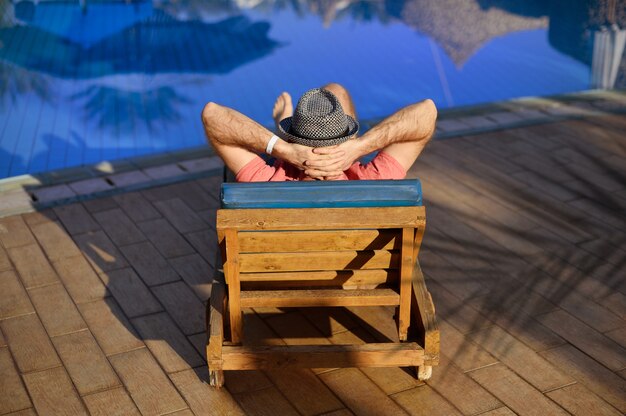 Relaxe na piscina de verão. Homem jovem e bem sucedido, deitado numa espreguiçadeira e levantando os braços