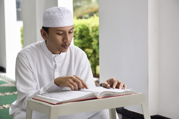 Religião homem muçulmano asiático com cap lendo livro sagrado alcorão