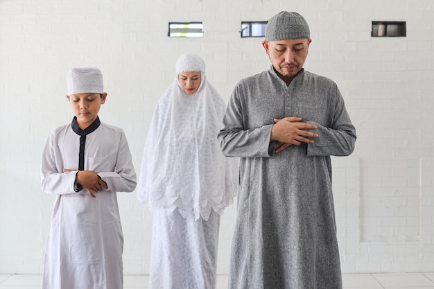 Religiöse asiatische muslimische Familie betet zusammen, steht mit der Hand in der Brust und macht Salat in der Moschee