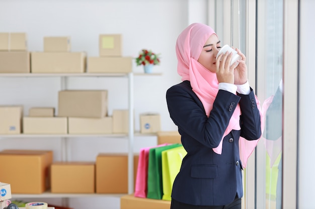 Religiöse asiatische muslimische Frau im blauen Anzug, der Kaffee, lächelnd und rosa Schal auf Kopf trinkt