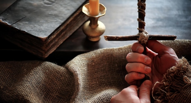 Religiöses altes Buch auf einem Holztisch. Ein religiöses Kreuz, das mit einem Seil und Sackleinen zusammengebunden ist, neben der Bibel. Verehren Sie Sünden und beten Sie
