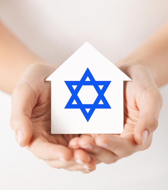 religión, judaísmo y concepto de caridad - manos femeninas sosteniendo una casa de papel con el símbolo de la estrella de david