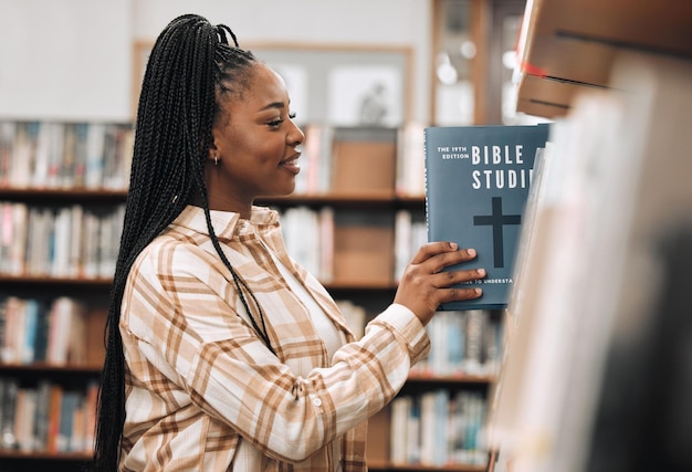 Religionsbucherziehung und schwarze Frau in einer Bibliothek für Forschungszwecke, die Gott und Wissen über die Bibel am College studieren Lernendes Lächeln und afrikanische Studentin mit Entscheidung über Bücher für ein Stipendium