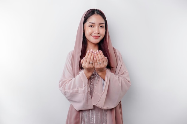 Religiosa hermosa musulmana asiática con un pañuelo en la cabeza rezando a Dios aislada de fondo blanco