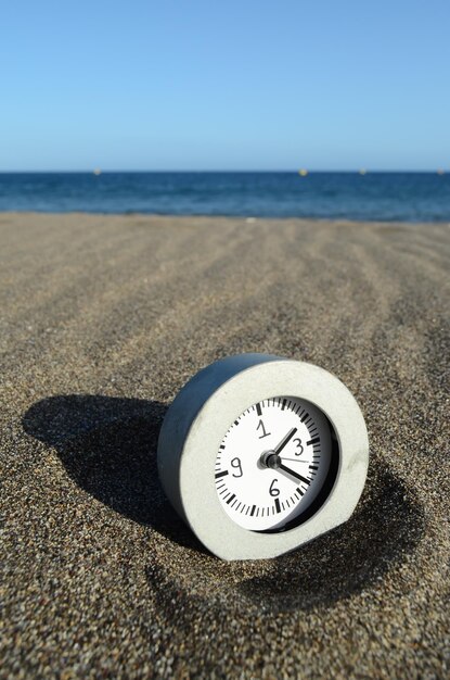 Relógio analógico clássico na areia na praia perto do oceano