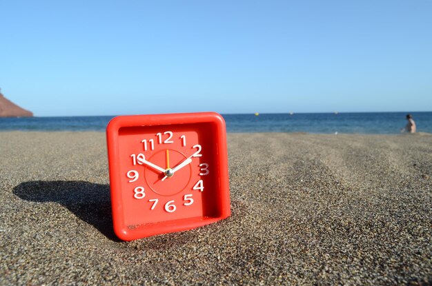 Relógio analógico clássico na areia na praia perto do oceano