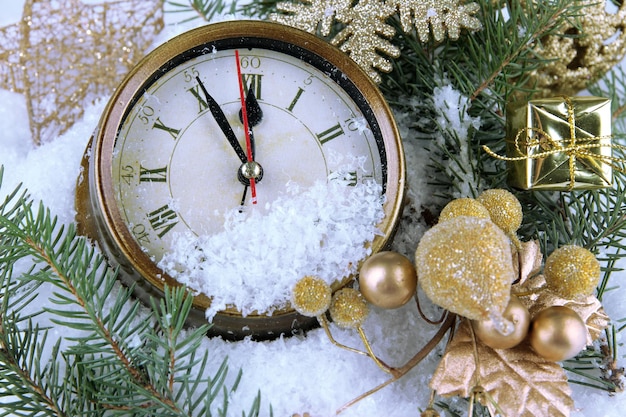 Relógio com galhos de pinheiro e decorações de Natal sob a neve de perto