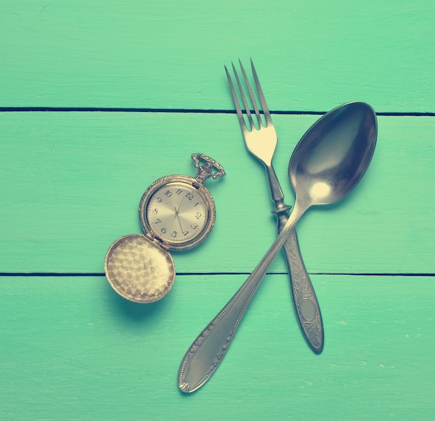 Relógio de bolso vintage, colher, garfo em uma mesa de madeira azul