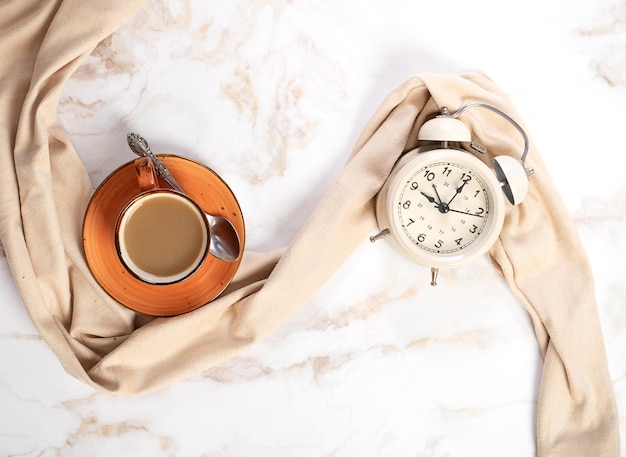 Relógio de xícara de café e despertador em uma mesa de mármore leve Rotina matinal lenta 9 da manhã