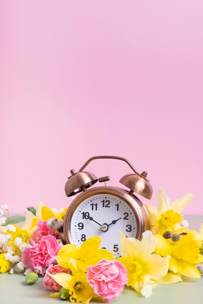 Relógio despertador com flores amarelas e cor-de-rosa Horário de primavera conceito de horário de verão primavera para a frente