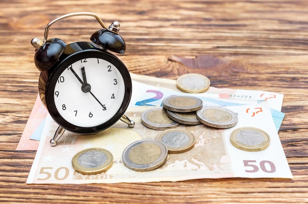 Relógio despertador com notas de euro e moedas na mesa de madeira Conceito de negócio