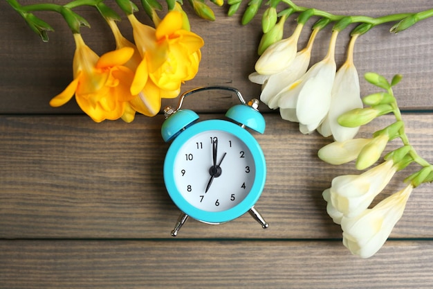 Relógio despertador e lindas flores sobre fundo azul de madeira