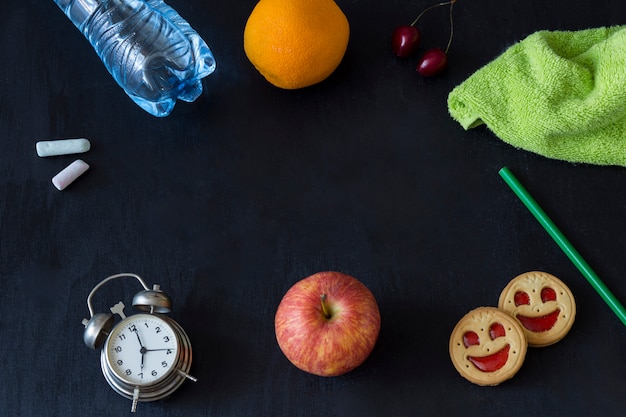 Relógio despertador, giz, maçã, biscoito, lápis, cereja, laranja, garrafa de água