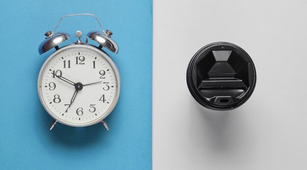 Relógio despertador, recipiente com café sobre fundo cinza azul. Vista do topo