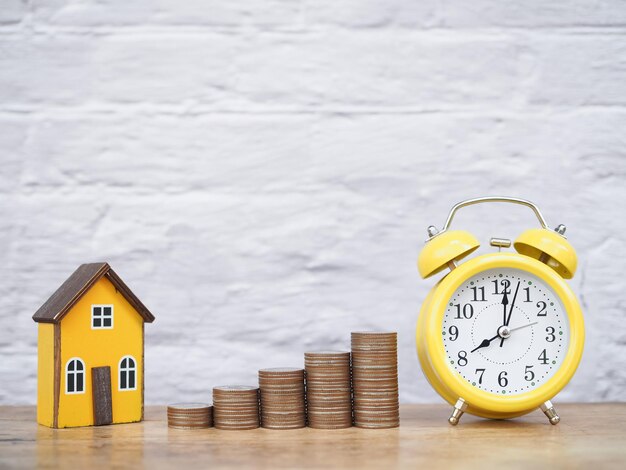 Foto reloj de alarma amarillo casa en miniatura y pila de monedas el concepto de ahorrar dinero para la casa administrar el tiempo para el éxito inversión inmobiliaria hipoteca de casa inmobiliaria