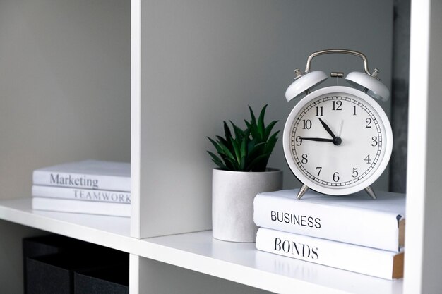 Foto reloj de alarma blanco con libros de negocios en los estantes de la oficina estrategia de negocios vender marketing