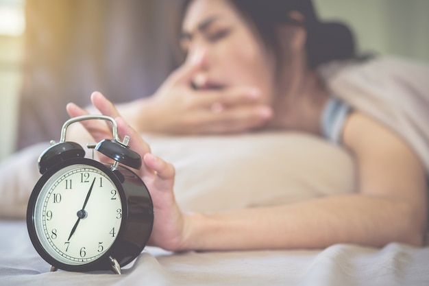 El reloj de alarma está sonando fuerte, con la mujer también dormida como el fondo borroso.