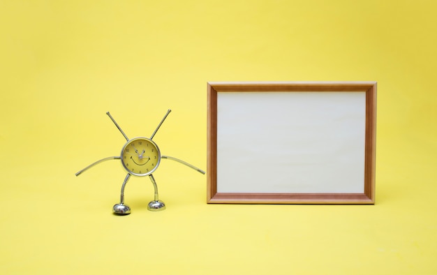 Foto un reloj amarillo y un marco con una sábana blanca vacía. reloj y marco en un espacio amarillo. reloj amarillo con forma de hombre.