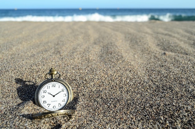 Reloj analógico clásico en la arena de la playa cerca del océano