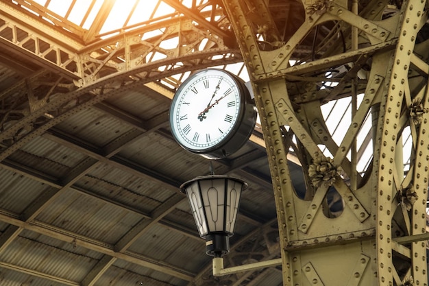 Reloj antiguo y linterna en la estación de tren con techo de edificio.