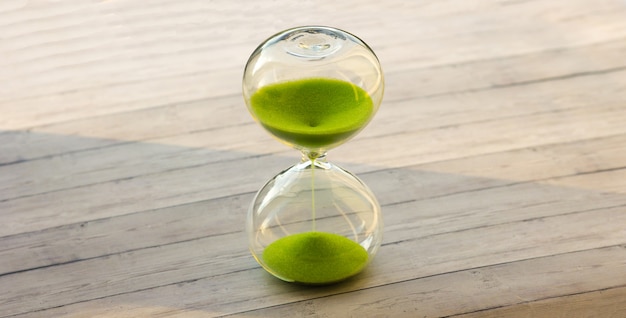 Reloj de arena con arena verde sobre un fondo de madera