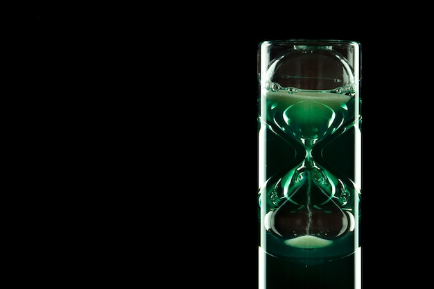 Foto reloj de arena de diseño moderno con líquido coloreado sobre un fondo oscuro.