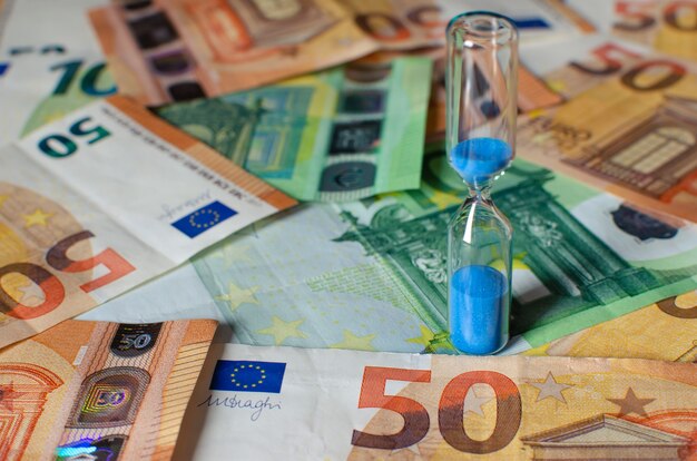 Reloj de arena en el fondo de los billetes en euros. Conceptos de inversión, rentabilidad, dinero de jubilación y movimiento de dinero a lo largo del tiempo