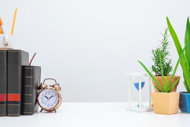 Reloj de arena, libro, reloj, agave, aloe vera y libro en la mesa de escritorio.