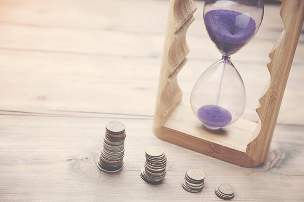 Reloj de arena con monedas en mesa de madera