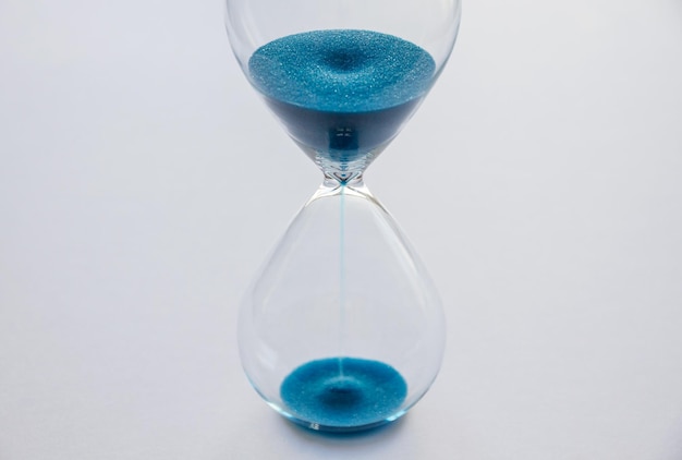 Reloj de arena que contiene arena azul aislada en un fondo blanco Concepto de paso del tiempo